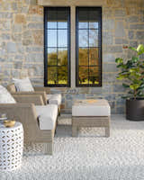 Outdoor living room with stone wall and gray Oved Area Rug, featuring neutral chairs and ottoman. Roomscene-Rectangle