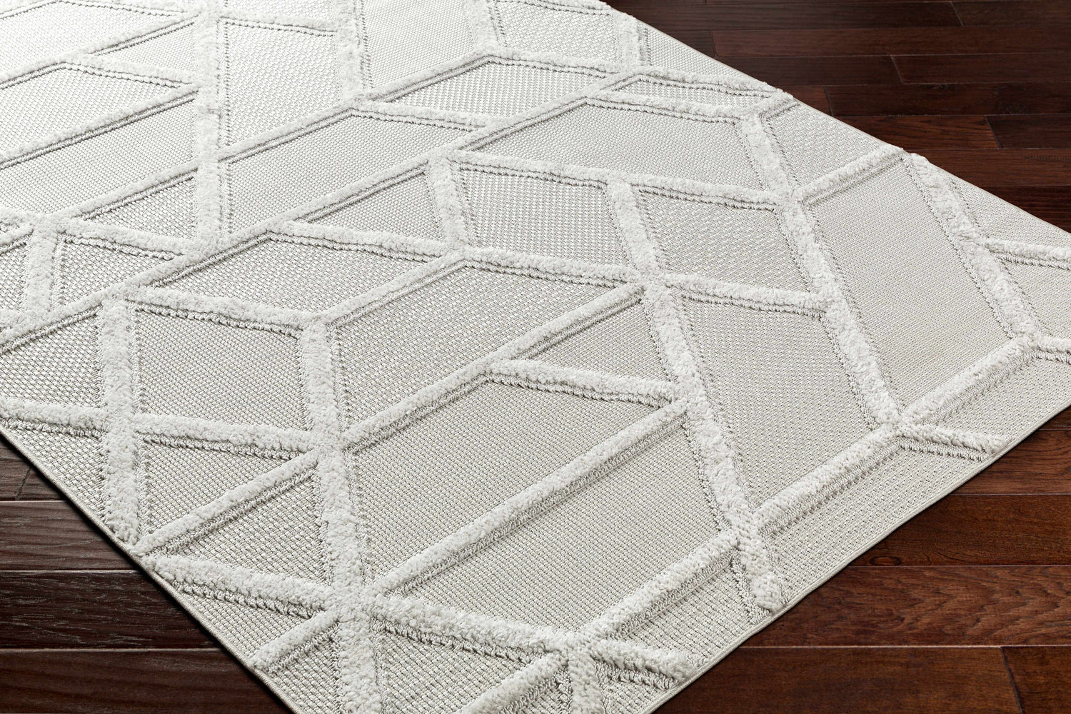 Close-up of Cadak Area Rug. Gray polypropylene rug with a geometric diamond pattern and a soft, textured pile. Corner