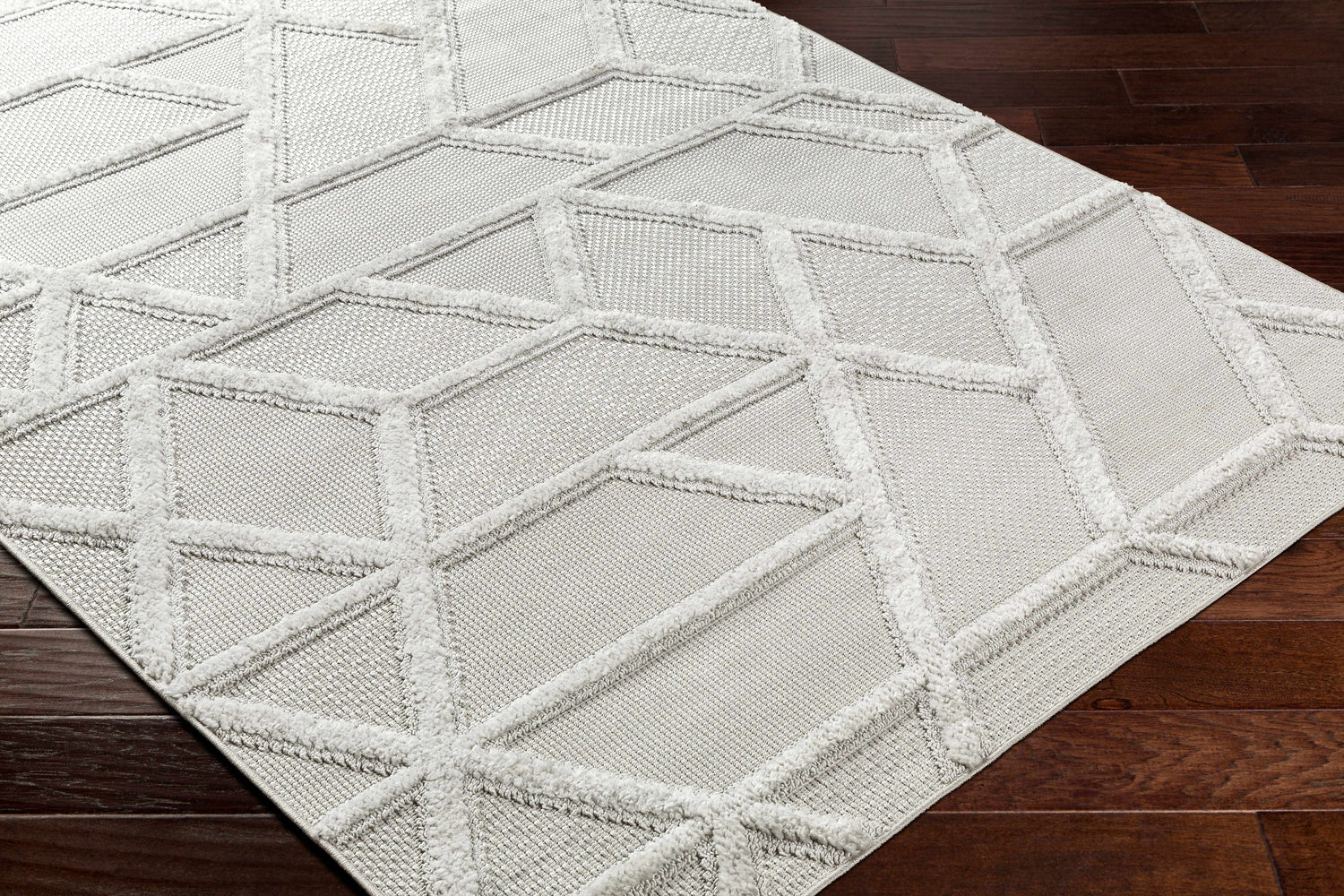 Close-up of the Cadak Area Rug. Gray rug with a geometric diamond pattern and soft, textured lines. Contemporary style. Corner