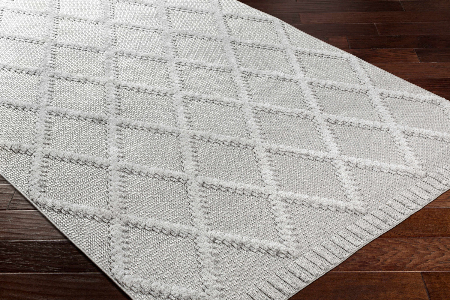 Close-up of the Galia Area Rug in arctic stone and gray, featuring a contemporary diamond pattern on dark wood floors. Corner