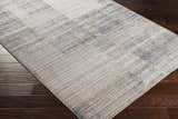 Close-up of the Sywell Luxe Fringe Rug in beige, blue, and tan, showing its linear pattern and soft texture on a dark wood floor. Corner