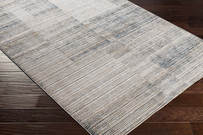 Close-up of the Sywell Luxe Fringe Rug in beige, blue, and tan, showing its linear pattern and soft texture on a dark wood floor. Corner