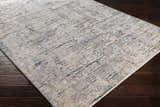 Close-up of Sywell Luxe Fringe Rug. Beige, blue, and charcoal abstract pattern on a soft polyester rug with fringe detail. Corner