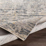 Close-up of the Sywell Luxe Fringe Rug showing its beige, blue, and charcoal contemporary pattern and soft polyester texture. Fold