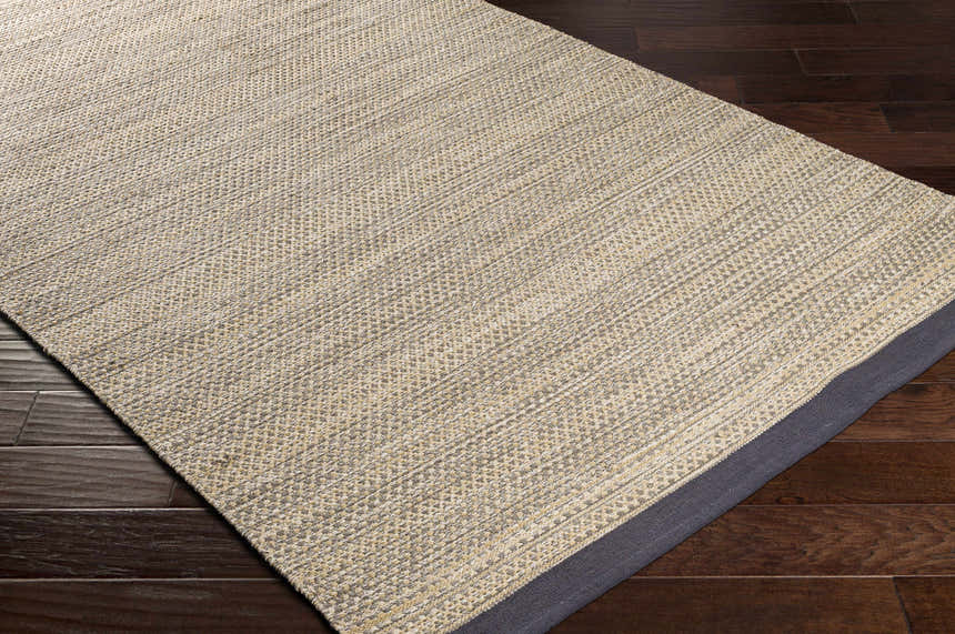 Close-up of Tanglewilde Area Carpet. Hand-woven cotton rug in beige, charcoal, and sage on dark wood floor. Southwestern style. Corner