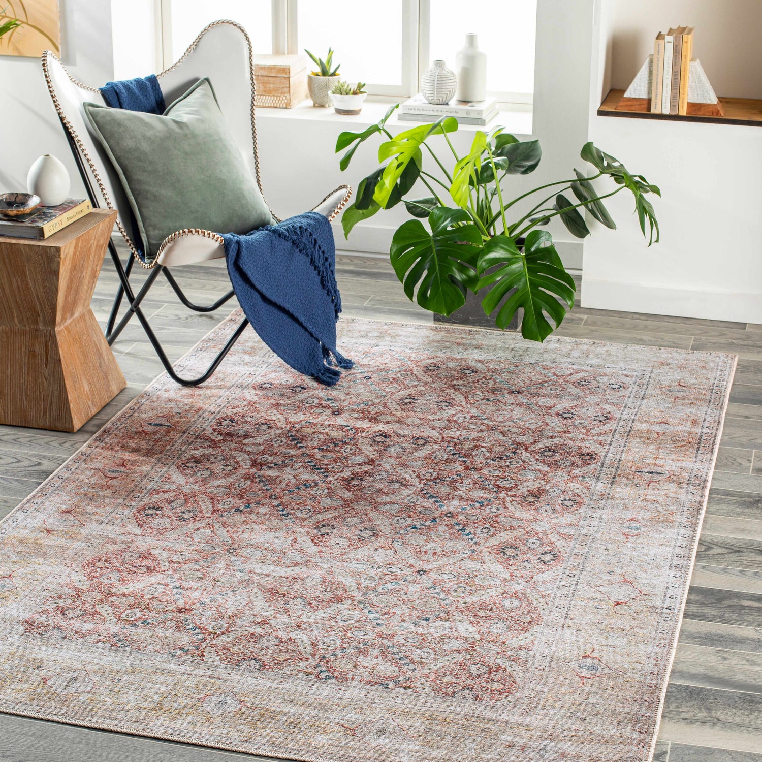 Living room scene with brick red and blue Tapia Washable Area Rug, butterfly chair, wood floors, and natural light. Roomscene-Rectangle