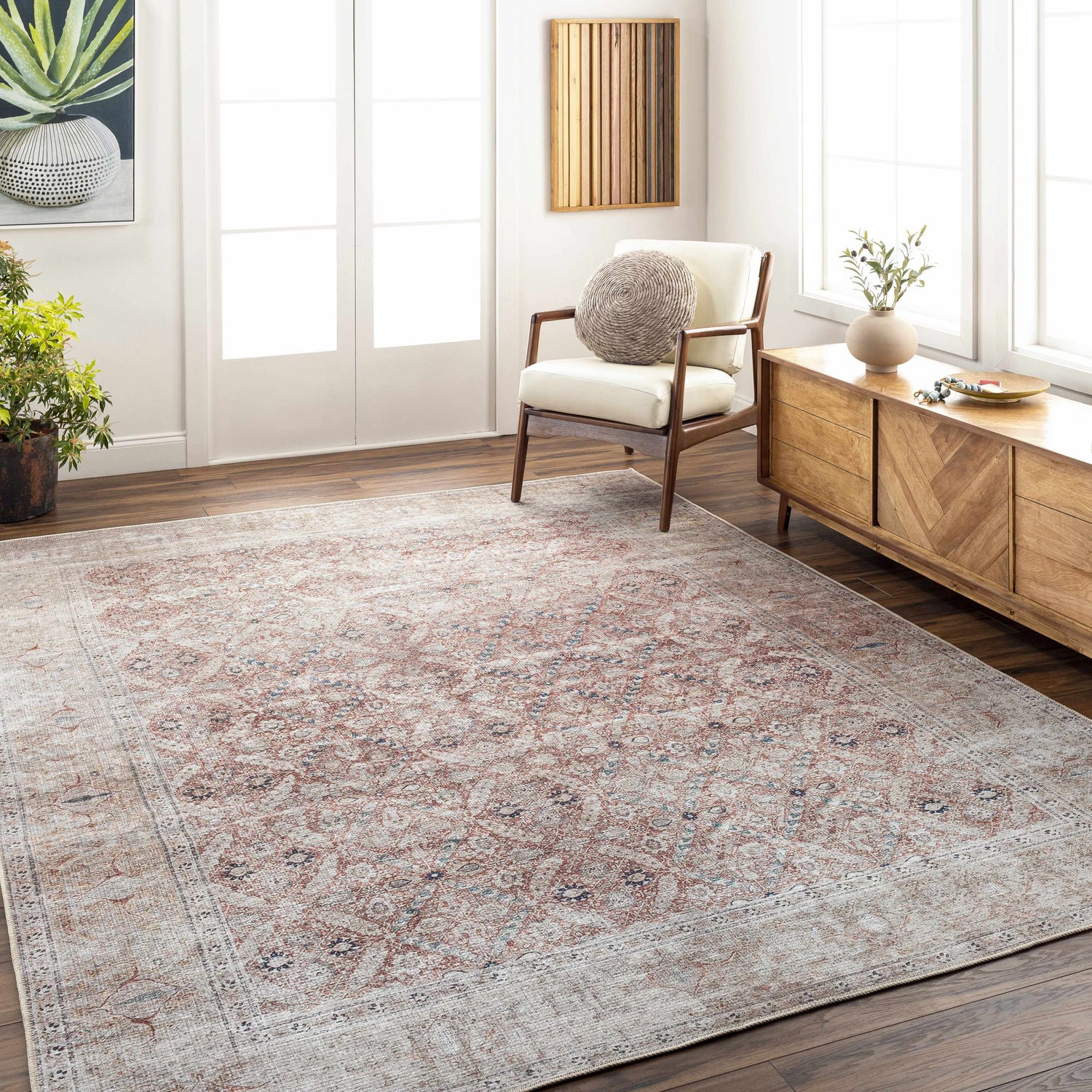 Living room scene with a brick red and dark blue Tapia Washable Area Rug, wood floors, white chair, and wood console table. Roomscene-Rectangle