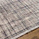 Close-up of the Taysan Area Rug. Features a dark gray, taupe, and mocha grid pattern with fringe detail. Texture