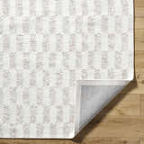 Close-up of the Theda Area Rug, a hand-tufted wool rug in ash, light silver, and off-white with a contemporary pattern. Fold