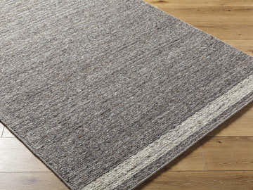 Close-up of the hand-tufted Tiran Gray Wool Area Rug showing texture and neutral gray tones with light wood floors. Corner
