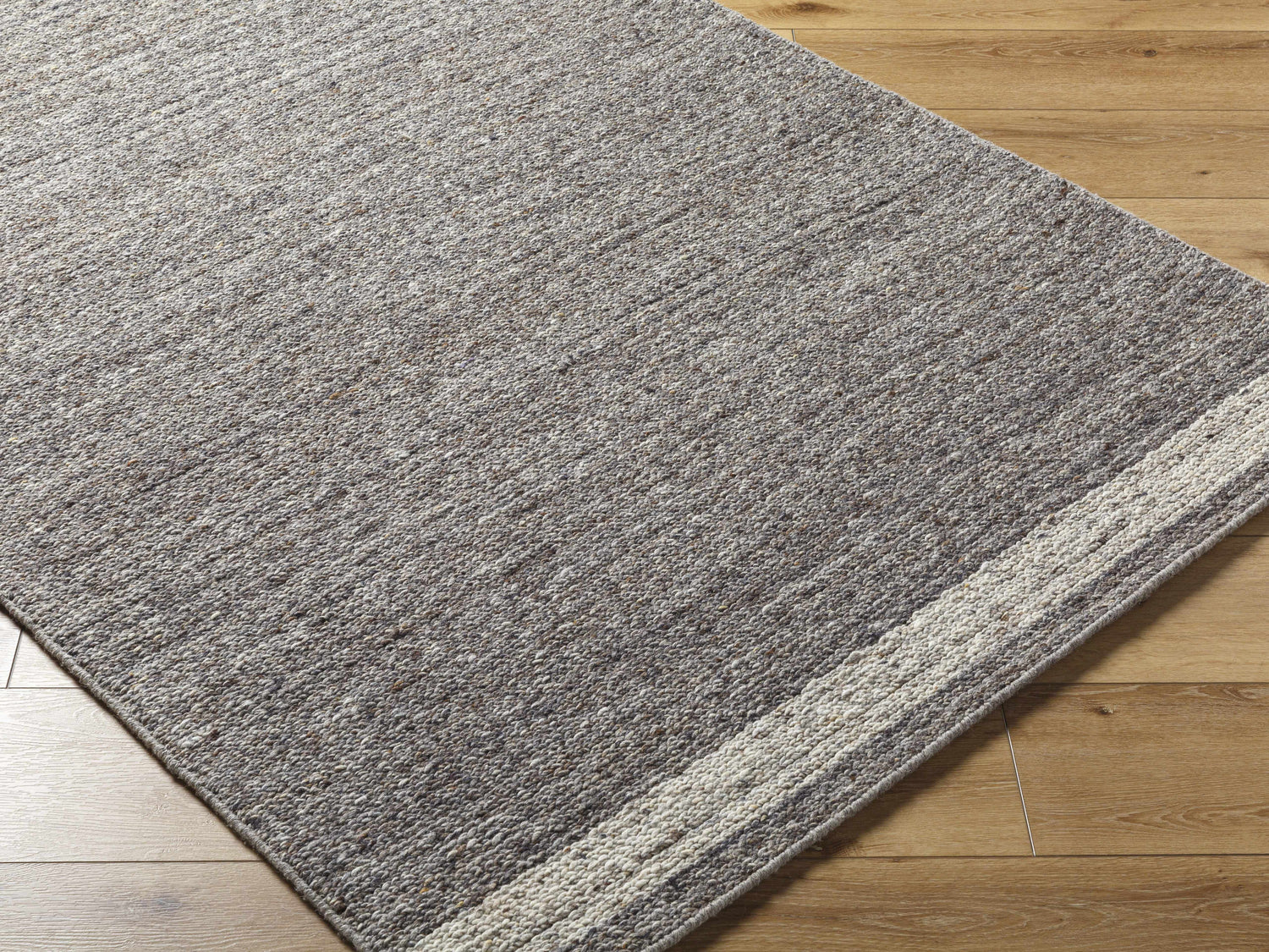 Close-up of the hand-tufted Tiran Gray Wool Area Rug showing texture and neutral gray tones with light wood floors. Corner