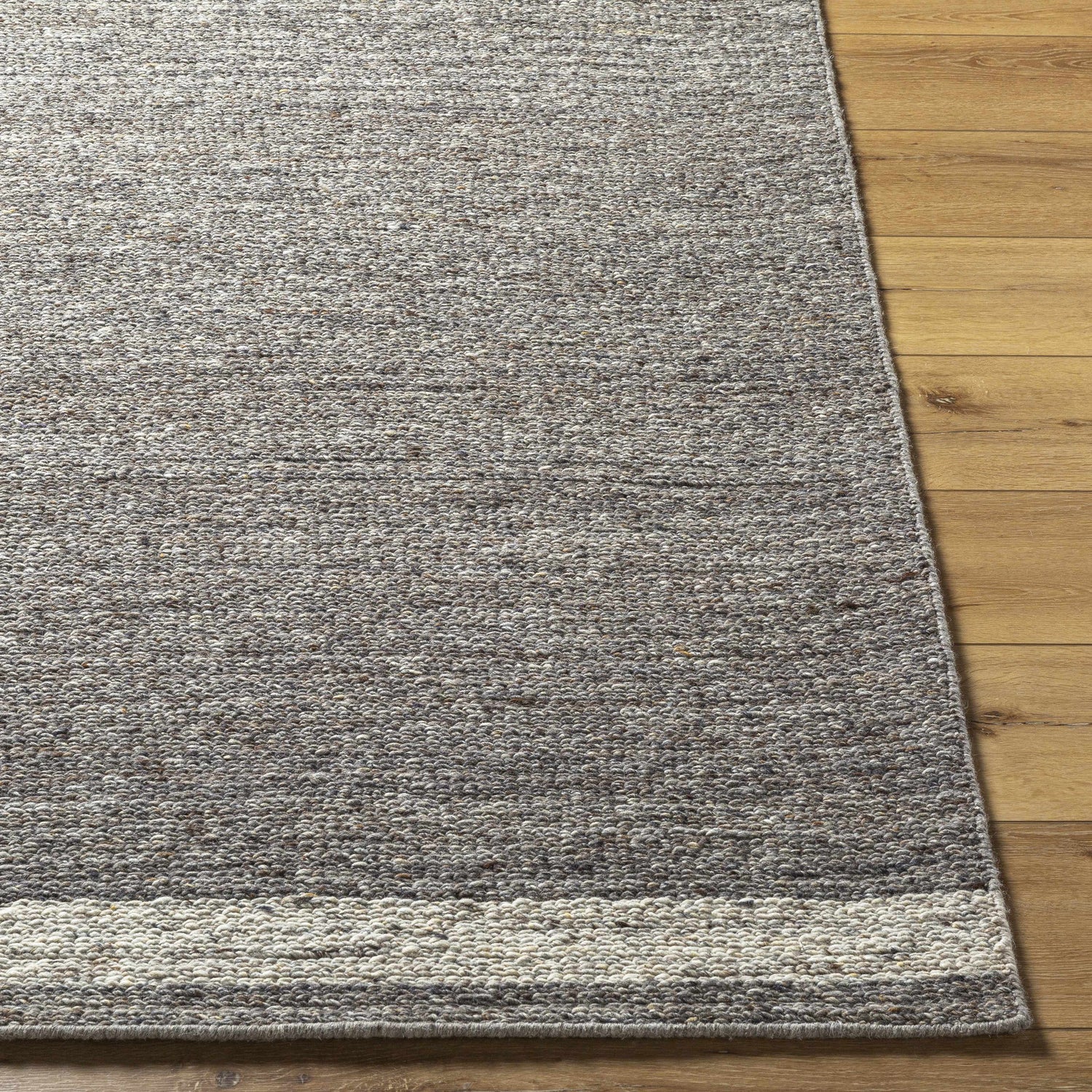 Close-up of the hand-tufted Tiran Gray Wool Area Rug showing texture and color variations on a wood floor. Front