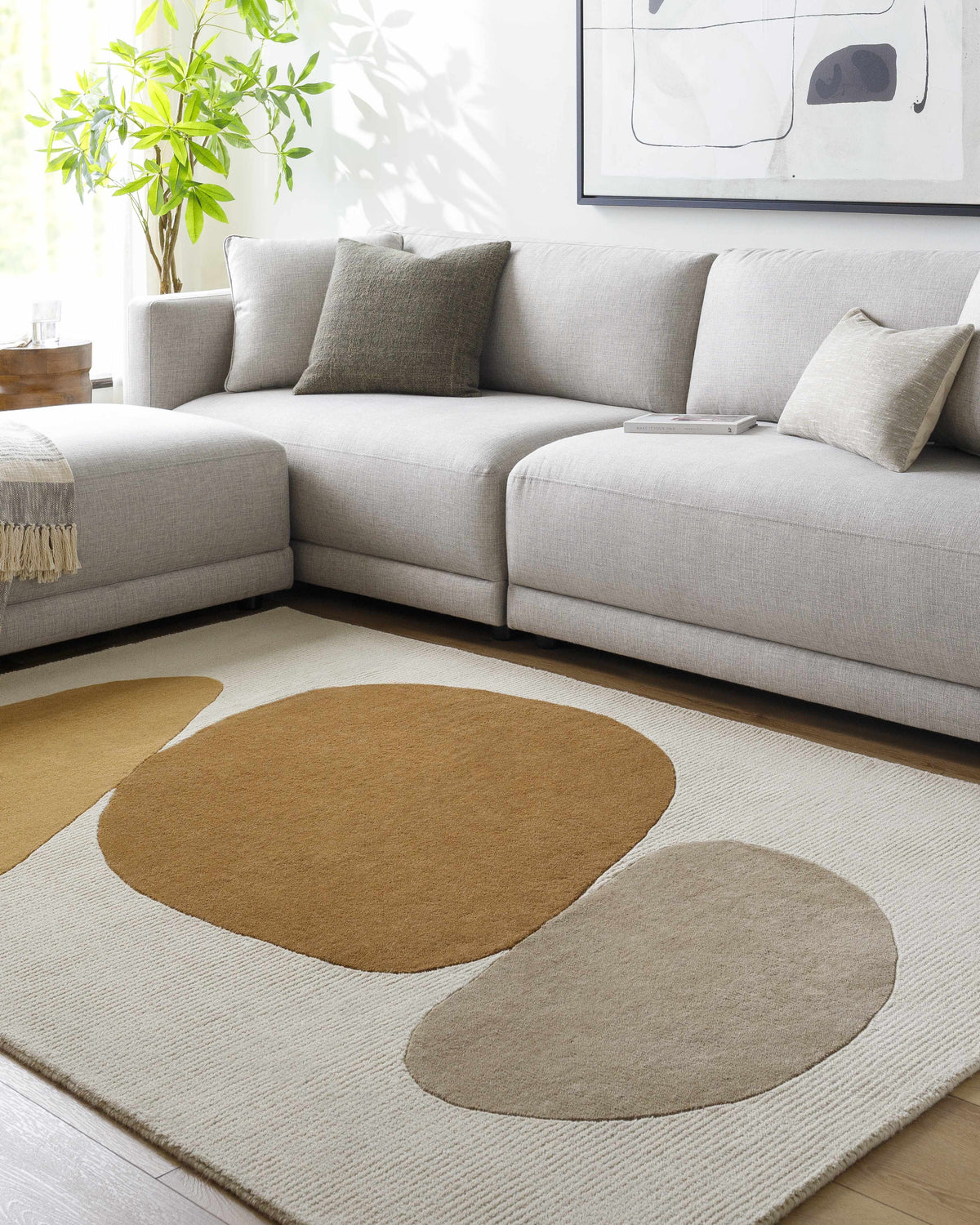 Living room scene with a gray sectional sofa and the Tutti Area Rug with tan, sepia, and brick red abstract shapes. Roomscene-Rectangle