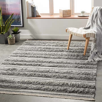 Living room scene with gray Teachey Carpet Area Rug, woven texture, neutral decor, wood chair, and herringbone throw. Roomscene-Rectangle