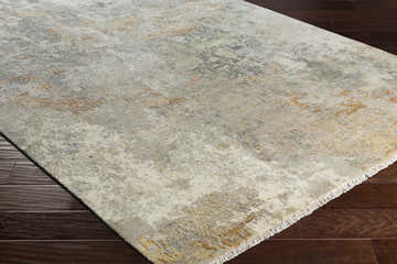 Close-up of the Telogia Carpet on dark wood floor. Contemporary style rug with gray, gold, and ivory abstract pattern. Corner