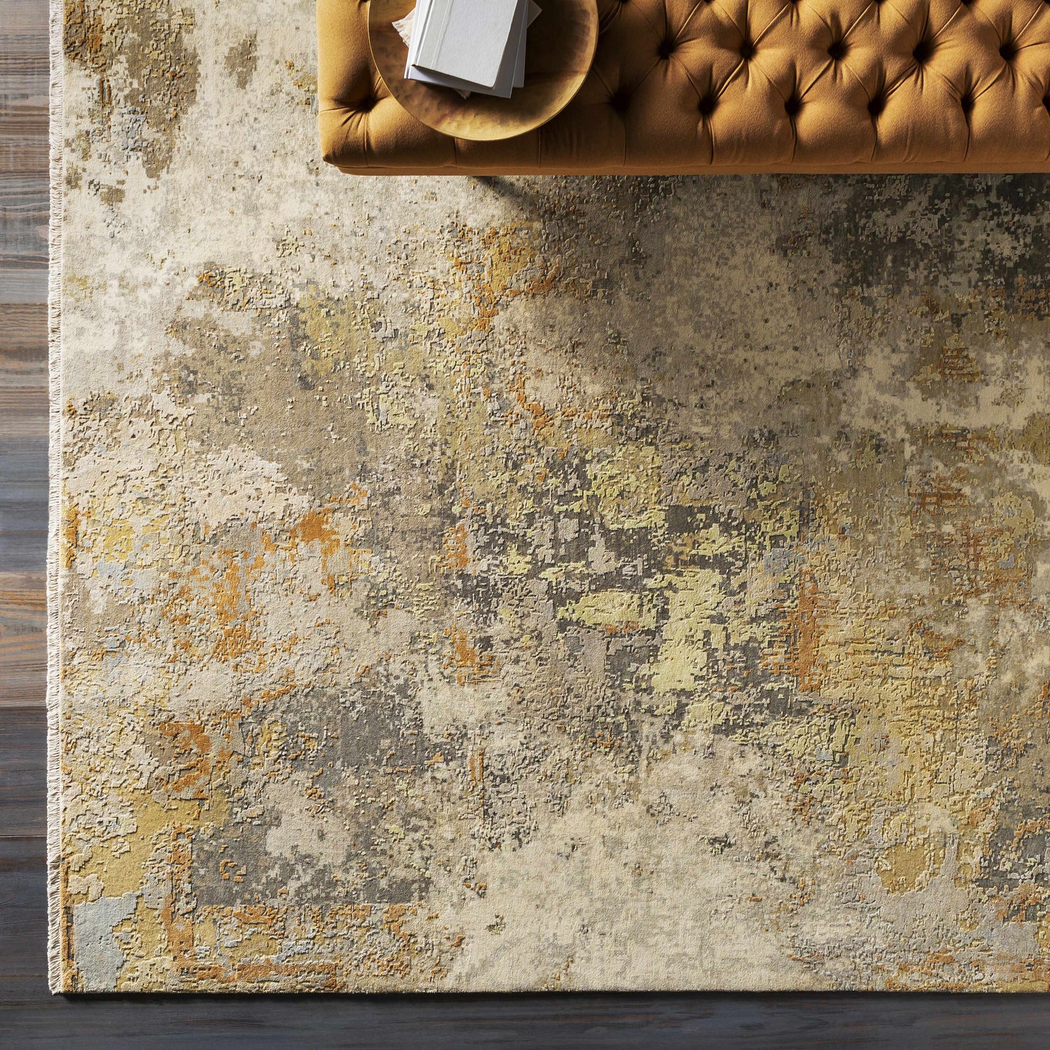 Overhead view of the Telogia Carpet. Contemporary wool rug with beige, gold, and gray distressed pattern. Tufted ottoman. Styleshot