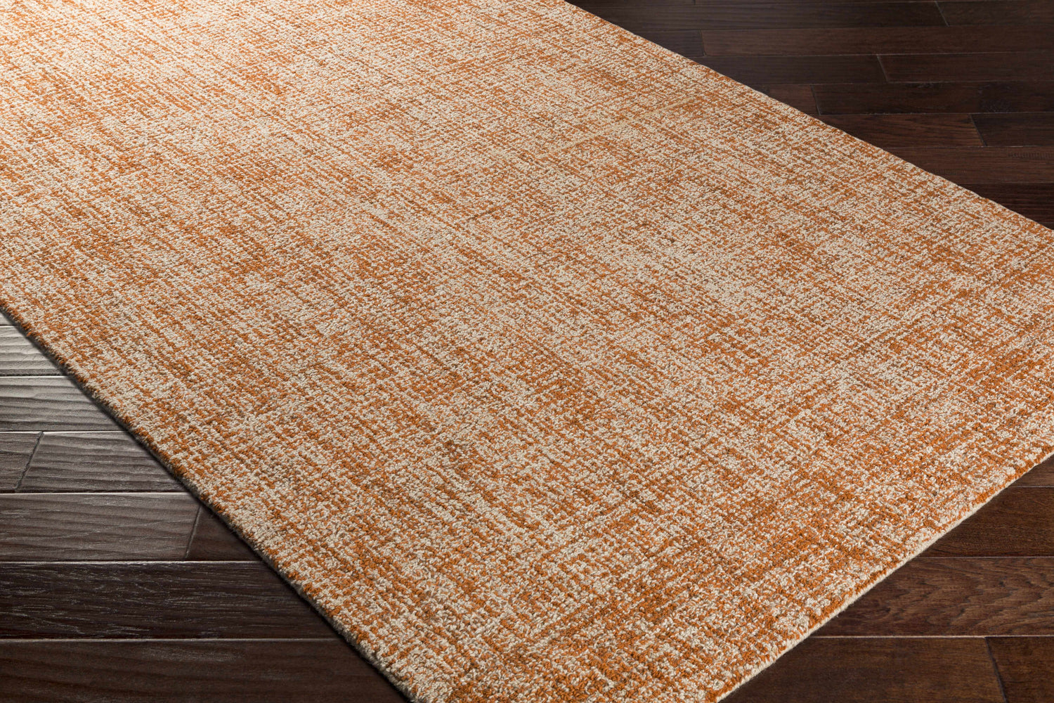 Close up of the Teresita Area Rug in burnt orange and ivory, a hand tufted wool rug on dark wood floors. Corner