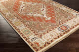 Angled view of the Texico Area Rug, a hand-knotted wool rug in farmhouse style, with orange, brown, and cream colors on dark wood flooring. Corner