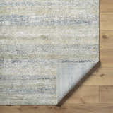 Close-up of the Taran Thick Luxe Rug showing light gray, olive, peach, and tan textured design on wood floor. Fold