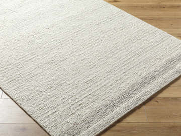 Close up of hand tufted Thady Area Rug. Ash, light silver, and pearl wool rug with subtle texture on wood floor. Corner