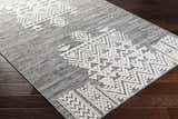 Close-up of the Thorntonville Outdoor Rug. Gray rug with a white geometric, bohemian pattern on dark wood floors. Corner