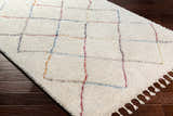 Close-up of the Tigao Area Rug on dark wood floor. Cream shag rug with black, orange, pink, and blue diamond pattern. Corner