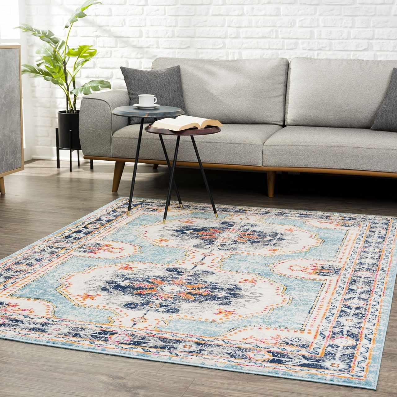 Living room scene with a Tigried Turquoise 2308 Area Rug, gray sofa, side tables, and a potted plant against a white brick wall. Roomscene-Rectangle