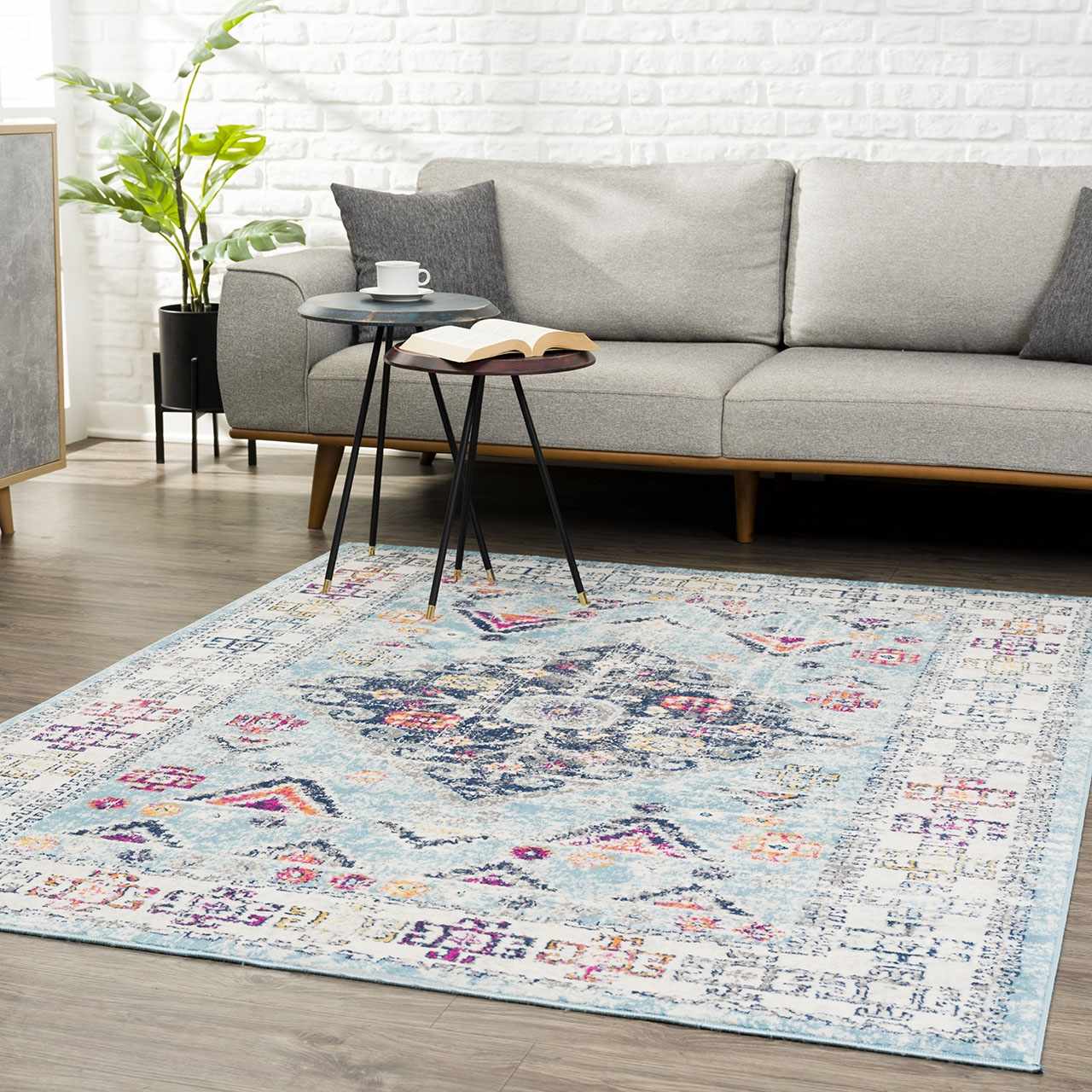 Living room scene with a Tigris Turquoise 2314 area rug, gray sofa, side tables, and a plant against a white brick wall. Roomscene-Rectangle