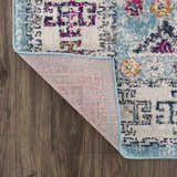 Close-up of the Tigris Turquoise 2314 rug showing its ivory, blue, pink, and orange bohemian pattern and machine-made backing. Fold
