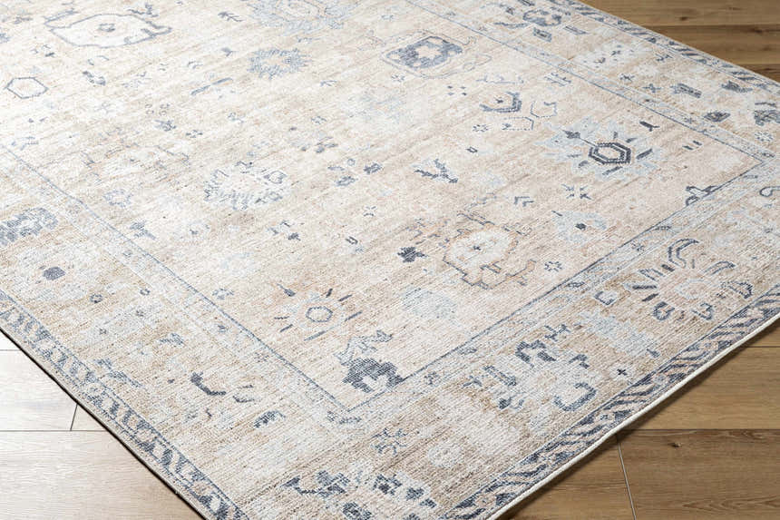 Close-up of the beige Toddy Area Rug with charcoal and slate blue traditional pattern on a wood floor. Corner