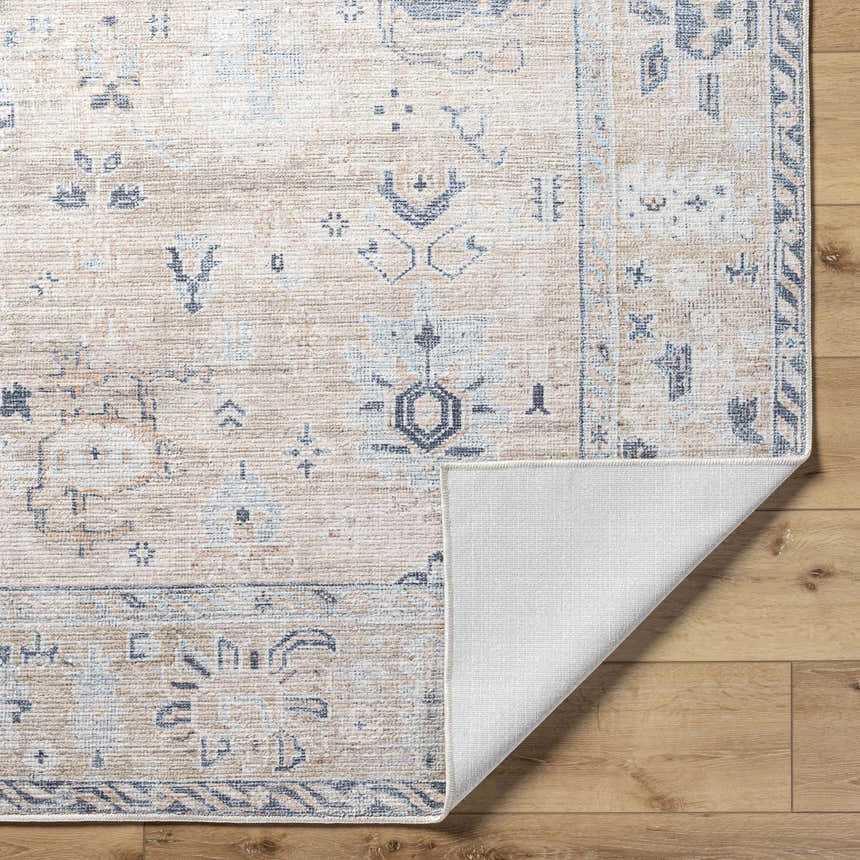 Close-up of the Toddy Area Rug, a beige rug with charcoal, mauve, and slate blue traditional patterns. Shows rug backing. Fold