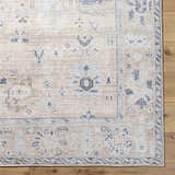 Close-up of the beige Toddy Area Rug with charcoal, mauve, and slate blue traditional pattern on a wood floor. Corner