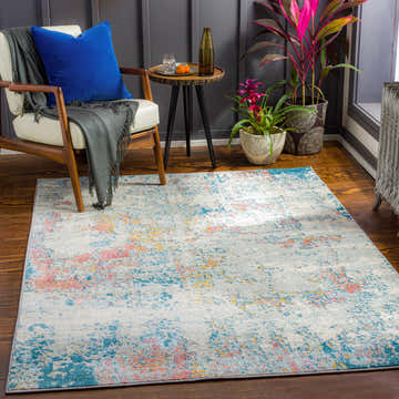 Living room scene with Tambalisa Abstract Area Rug, cream chair, blue pillow, plants, and wood floors. Roomscene-Rectangle