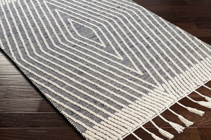 Close-up of the Tamayong Tasseled Jute&Wool Rug. Cream tassels accent the black and cream striped, hand-woven rug. Corner