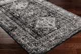 Close-up of the Toni Area Rug in black and gray, showcasing its traditional, distressed pattern and soft texture on wood floor. Corner