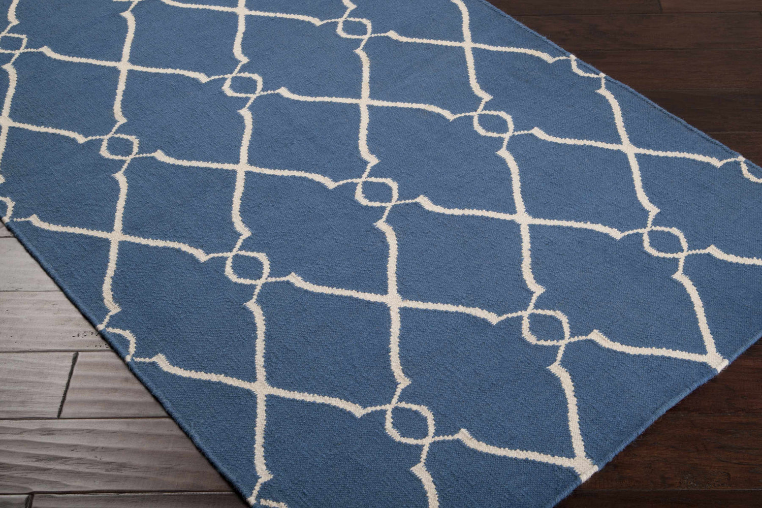 Close-up of the Toccopola Area Carpet. Dark blue wool rug with a light beige geometric trellis pattern. Hand woven texture. Corner