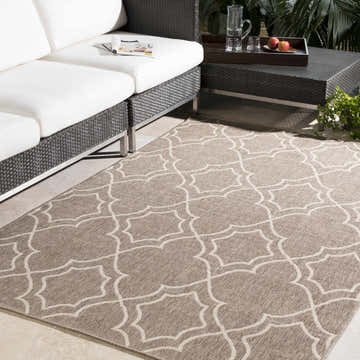 Outdoor patio scene with a brown and beige geometric Toledo Area Rug, white sofa, and dark wicker table. Roomscene-Rectangle