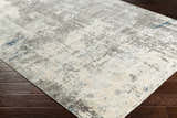 Close-up of the Tonalea Carved Statement Area Rug. Abstract pattern in ivory, gray, charcoal, and blue on dark wood floors. Corner