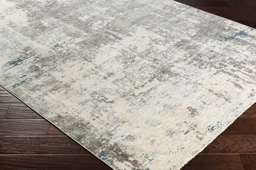 Close-up of the Tonalea Carved Statement Area Rug. Abstract pattern in ivory, gray, charcoal, and blue on dark wood floors. Corner