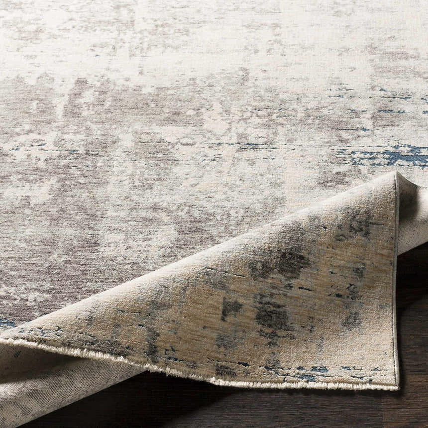 Close-up of the Tonalea Carved Statement Area Rug showing its ivory, gray, and blue abstract pattern and carved texture. Fold