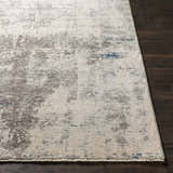 Close-up of the Tonalea Carved Statement Area Rug. Abstract pattern in ivory, gray, and blue on a dark wood floor. Front