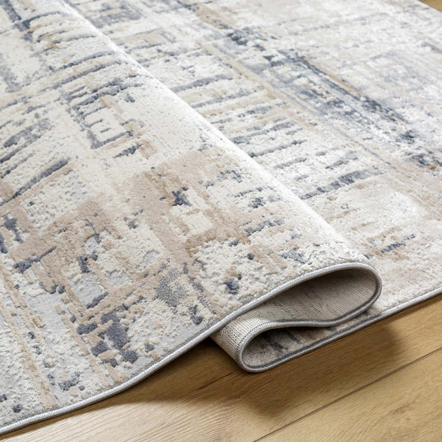 Close-up of the Tut Textured Luxe Rug showing its charcoal, ivory, beige, and gray contemporary design and soft texture. Fold