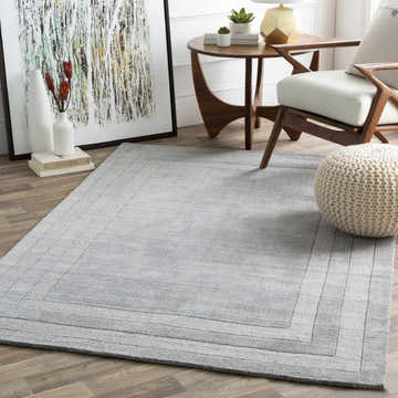 Living room scene with gray Turbotville area rug, wood floors, modern chair, round side table, and abstract art. Roomscene-Rectangle
