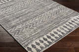 Close up of the Tuy Area Rug showing the dark gray bohemian-inspired geometric pattern and distressed texture. Corner