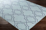 Close up of the Ursa Area Rug in pale blue with a navy quatrefoil pattern on dark wood flooring. Corner