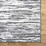 Close up of Vembo Area Rug with a contemporary black, gray, and light silver striped pattern on wood floor. Corner