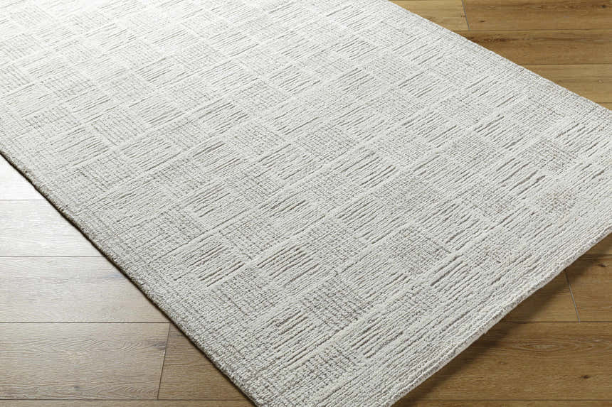Close-up of the Urian Area Rug, a hand-tufted wool rug in light silver and silver gray with a contemporary geometric pattern. Corner
