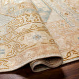 Close-up of the hand-knotted Villareal Area Rug, featuring cream, dusty pink, ice blue, and mustard hues. Wool texture visible. Fold