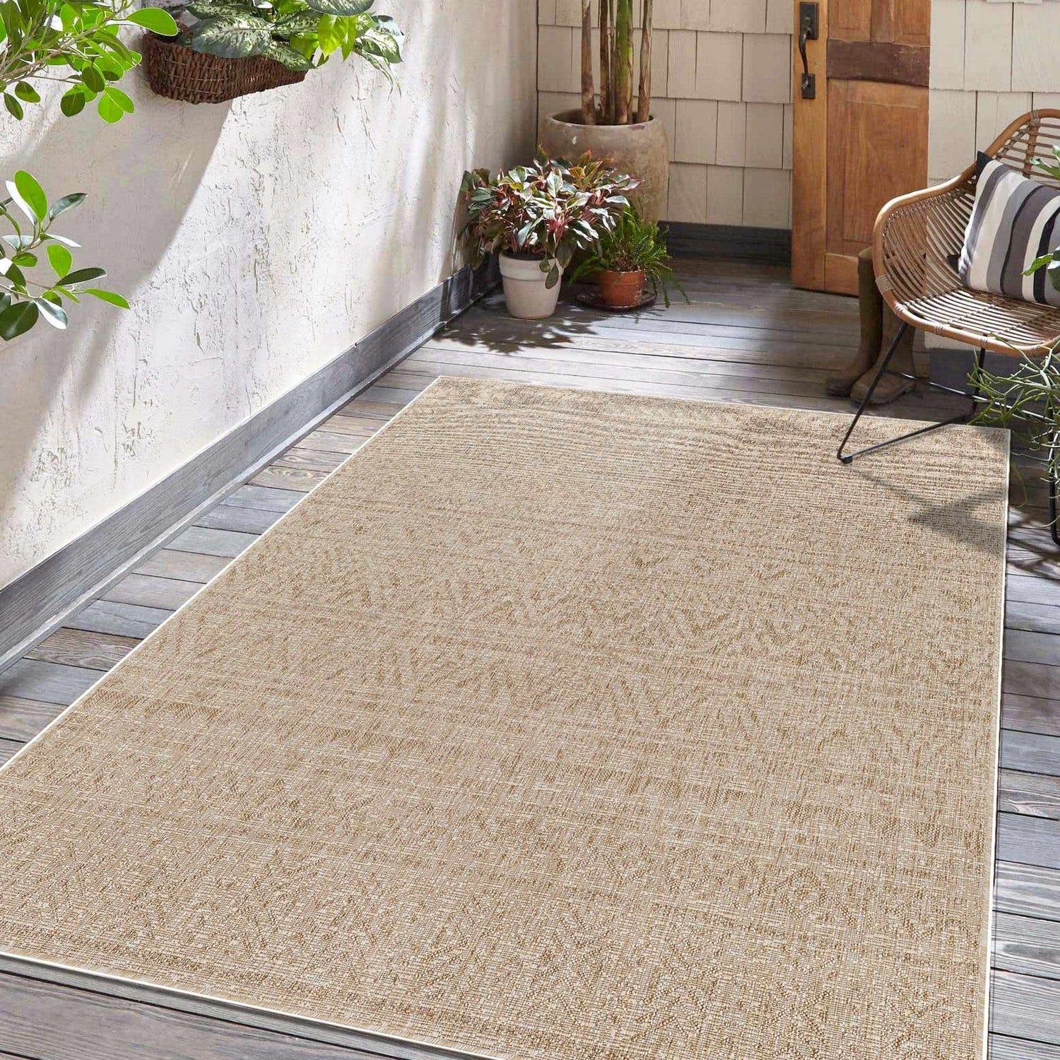 Covered porch with a light peach Vanderhoof Indoor Outdoor Rug, wicker chair, plants, and wood door. Roomscene-Rectangle