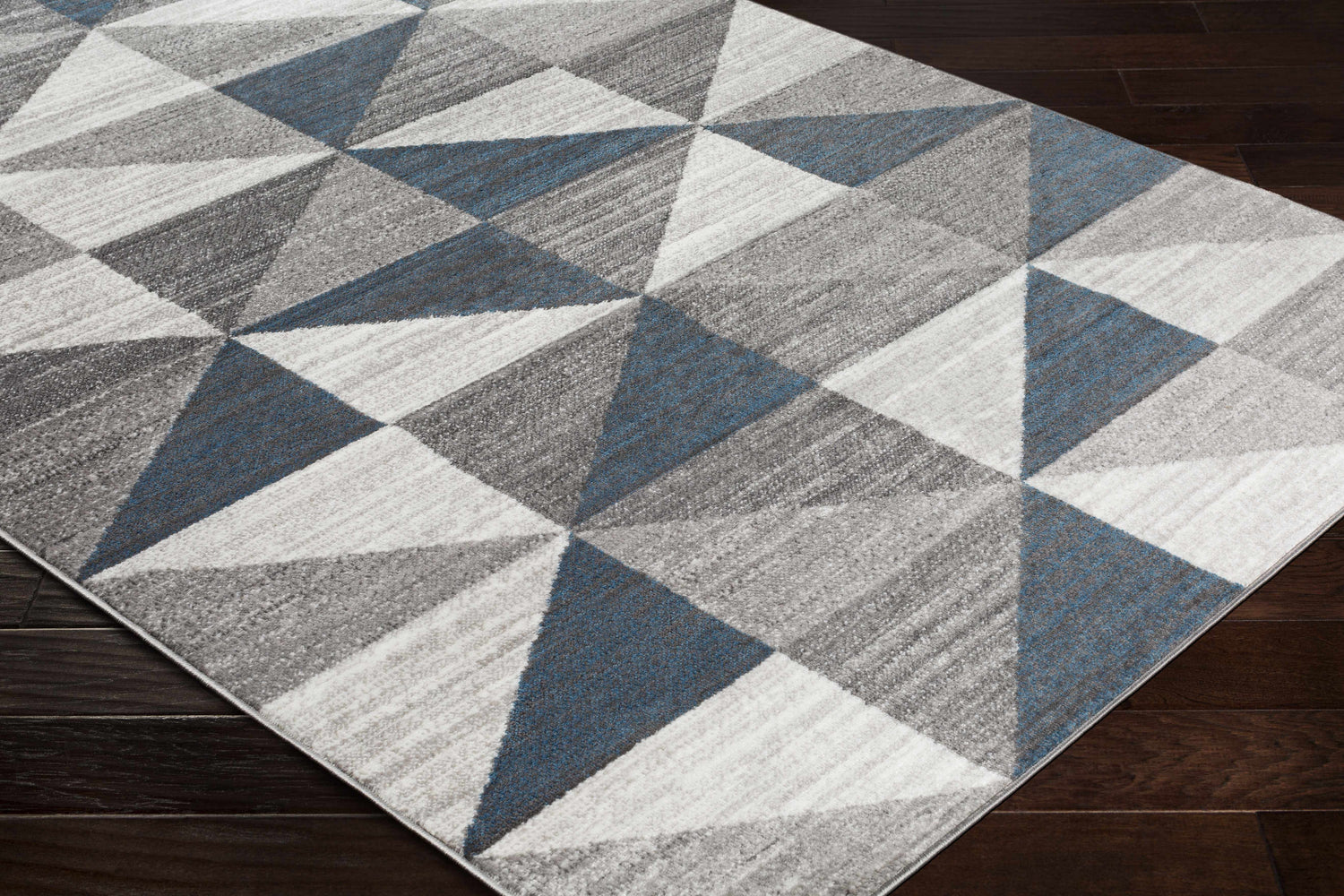 Close-up of the Volant Area Rug showcasing its blue, gray, and white geometric triangle pattern and soft texture. Corner